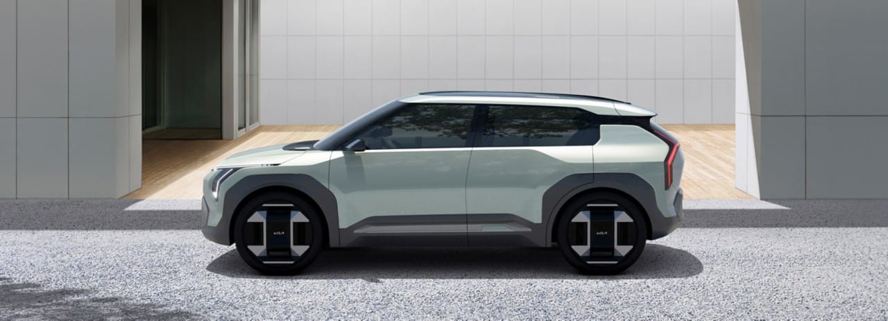Vehículo conceptual Kia EV3 en verde claro, vista lateral, estacionado fuera de un edificio con un parabrisas envolvente que da la ilusión de un techo flotante.