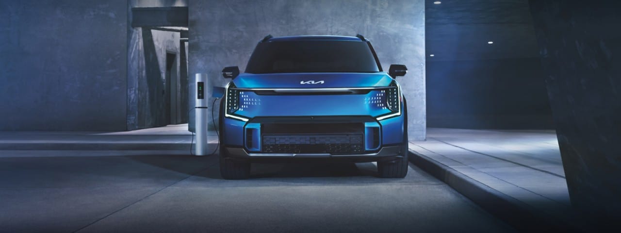 2024 Kia EV9 in blue, being charged while the owner is away in a modern building, front view
