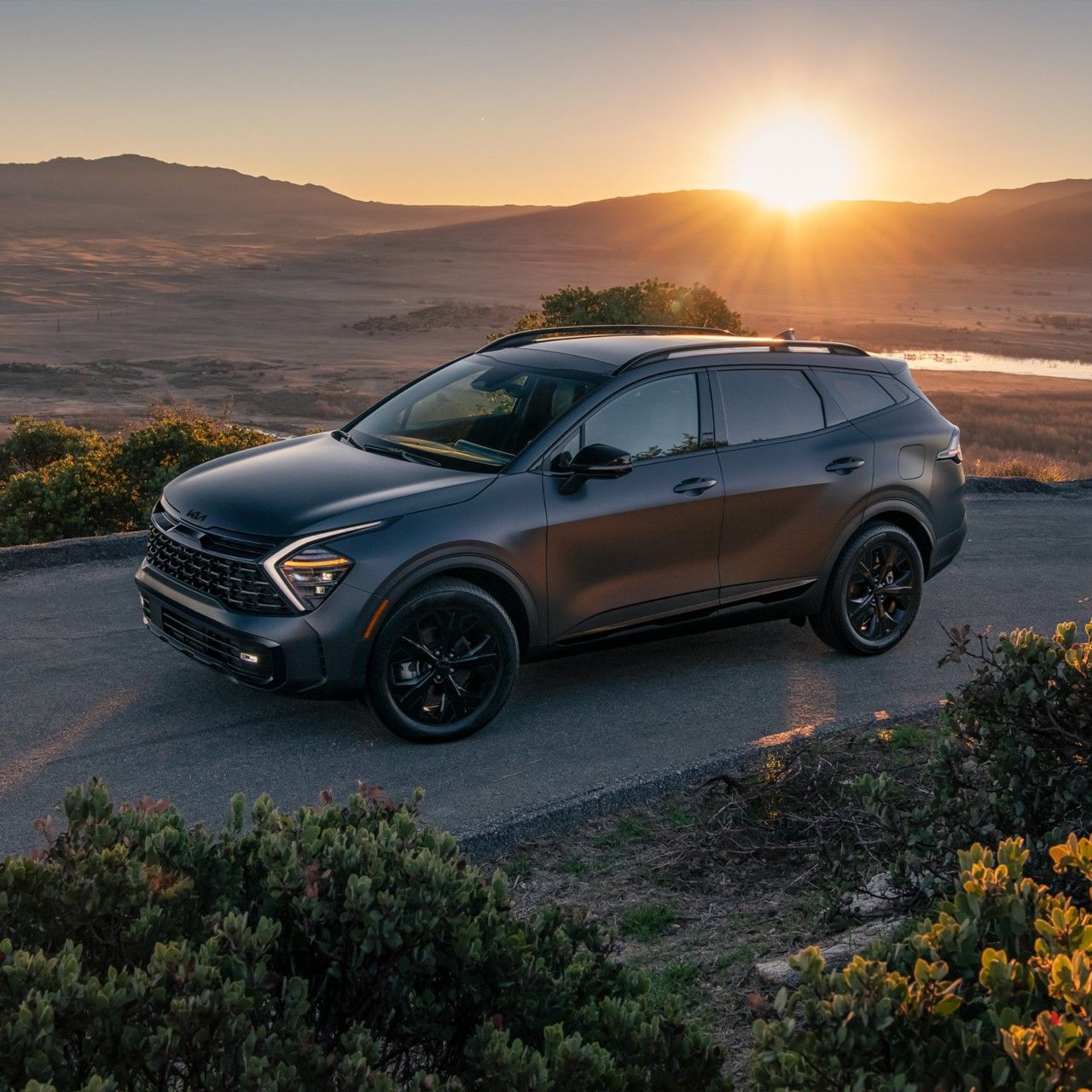 Vista lateral de tres cuartos del lado del conductor del Kia Sportage Plug-in Hybrid 2025 estacionado en una carretera en el valle
