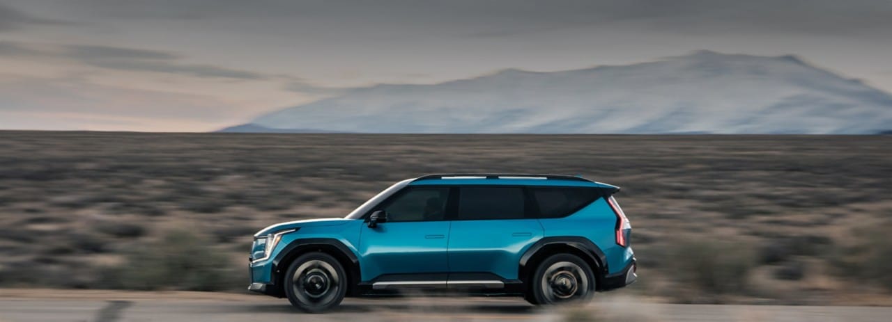 Perfil izquierdo de un EV9 azul conduciendo por una carretera desértica