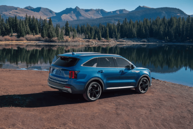  2025 Kia Sorento Hybrid in blue, three-quarter back view, parked in front of a lake in the forest