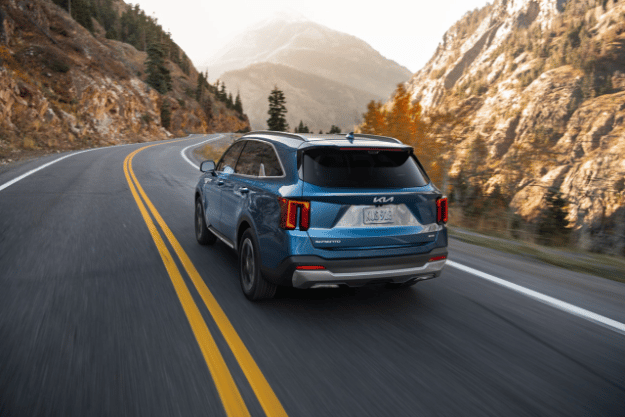  2025 Kia Sorento Hybrid in blue, three-quarter back view, driving through a mountain road