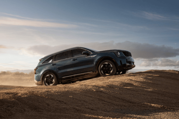 2025 Kia Sorento Hybrid in blue, three-quarter front view, driving up a mound of sand in the desert