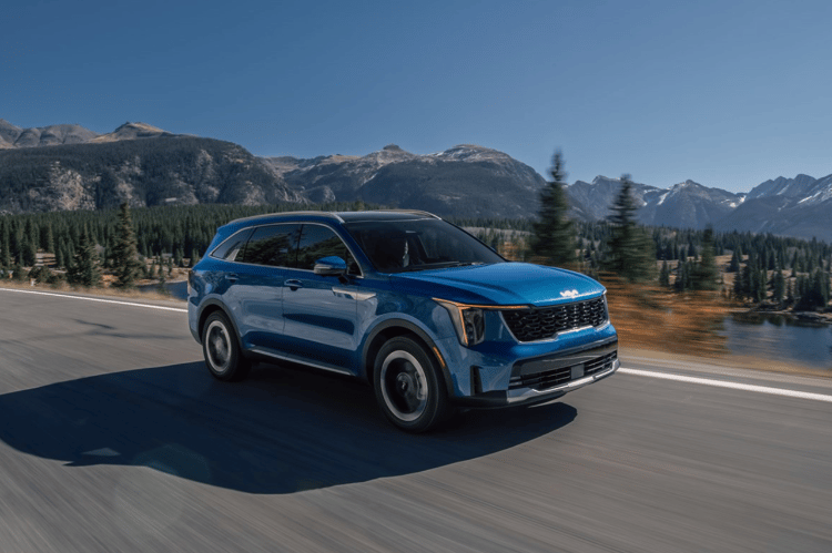  2025 Kia Sorento Hybrid in blue, three-quarter front view, driving on a road by the forest