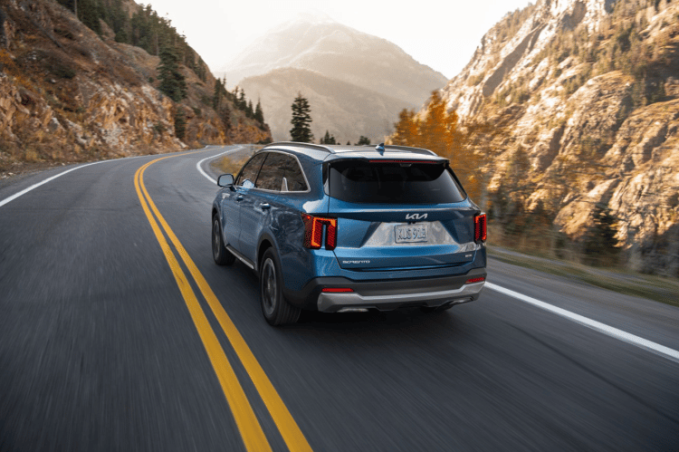  2025 Kia Sorento Hybrid in blue, three-quarter back view, driving through a mountain road