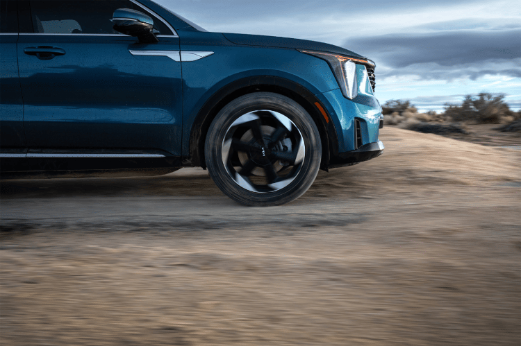 2025 Kia Sorento Hybrid in blue, front view, driving through a puddle of mud in the dessert making a big splash