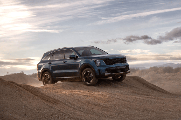2025 Kia Sorento Hybrid in blue, three-quarter front view, driving over mounds of sand in the desert